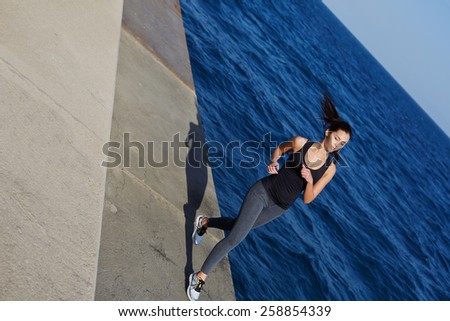 Full length portrait of athletic woman with beautiful figure running next to the ocean at sunny day, dynamic picture with sport girl working out with flying hair in action