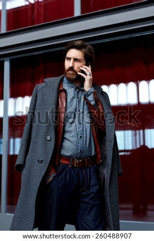 Portrait os stylish fashionable man in elegant coat having phone conversation walking in beautiful hotel hall