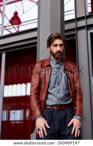 Portrait of hipster man with beard posing indoor while leaning on interior building pillar looking away
