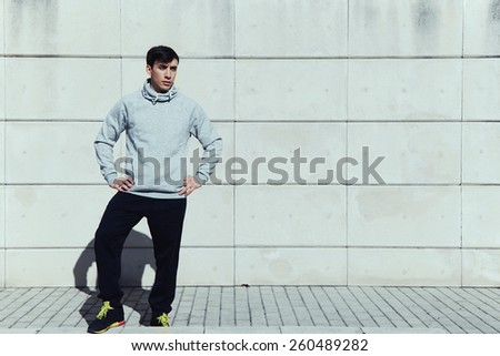 Full length portrait of young athletic man in sportswear standing against white brick wall background at sunny day, ready to workout and exercise, filtered image