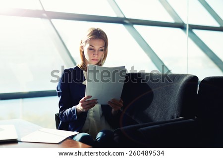 Half length portrait of female managing director examining paperwork in bight light office interior, attractive business woman read some documents before meeting, soft focus, filtered image