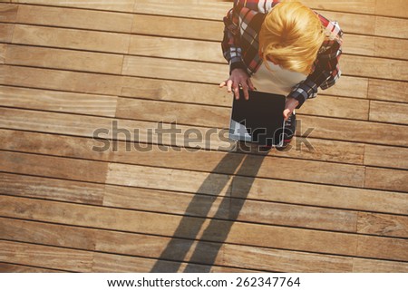 Top view blonde hair young woman using digital tablet with with a blank screen standing on wooden floor with copy space area background, young freelancer using busy tablet outdoors