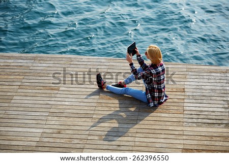 High angle shot of young tourist woman taking a photo of a beautiful view with her camera tablet, cute hipster girl relaxing at her sunny holiday photographing outdoors, young woman on sea pier
