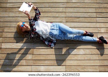 High angle shot of a pretty young woman pouting for a self-portrait while lying on wooden jetty enjoying the sun, cute tourist girl taking self-ie with digital tablet camera outdoors