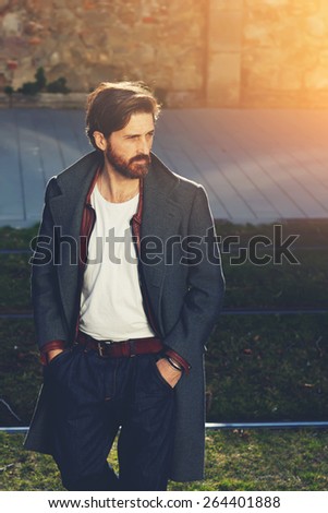 Portrait of elegant fashionable adult man dressed in coat walking on tram-line in urban setting, stylish hipster man walking on the street at sunny evening, flare sunshine