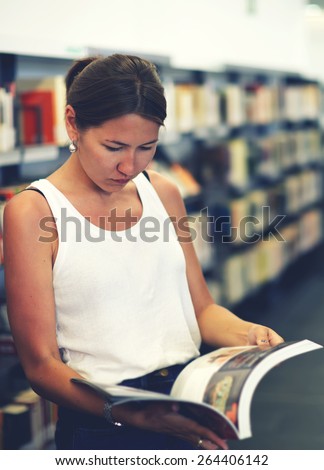 Portrait of young asian female holding open magazine or book while standing near bookshelves, attractive chinese student girl read book in university library, female freelancer in co-working space