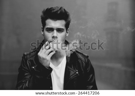 Close up portrait of handsome masculine model smoking cigarette and exhaling the fume, trendy attractive man blowing smoke out of his mouth, black and white filter,vintage effect
