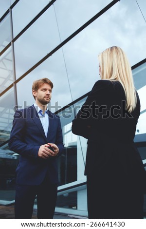 Rear view managing businesswoman with crossed arms standing opposite smiling employee outside office, business colleagues having conversation or discussion, businessman with cellphone talking to boss