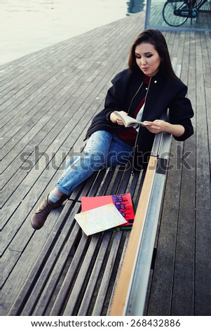 Vacation holiday in Barcelona, young female traveler sitting on wooden bench read some book, Chinese student girl reading book sitting in sea port on wooden pier, travel and leisure concept