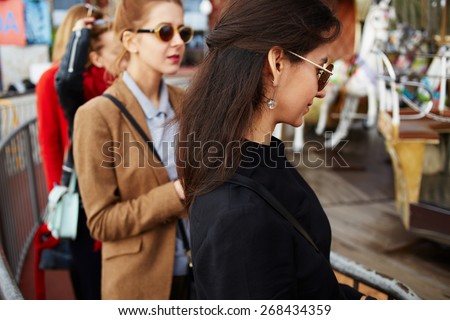 Girlfriends queuing for tickets to ride on carousel in amusement park during their holidays