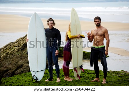 Group of tree professional surfers standing on the beach, blonde california girl, sexy muscular brunette man and red hair handsome man, summer holidays on surf camp