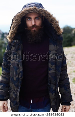 Portrait of stylish hipster model with red beard and beautiful blue eyes looking to the camera standing outdoors