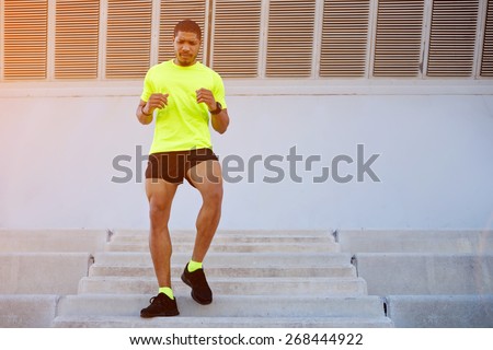 Full length portrait of sporty young man running down a flight of stairs while training outdoors at sunny afternoon,male runner dressed in bright t-shirt working out outdoors while doing legs exercise