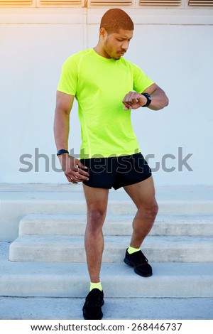 Full length portrait of male runner looking at his watch while going for a run at sunny afternoon,sporty young man dressed in bright t-shirt with space for your text message checking his time outdoors