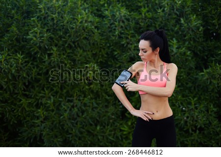 Sporty young woman standing in the park with big copy space for text while getting ready for workout,healthy fit runner setting her personal trainer application or stopwatch on cell phone before a run