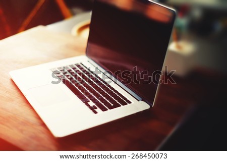 Workplace with open laptop with black screen on modern wooden desk, angled notebook on table in home interior, filtered image, cross process, focus on keyboard