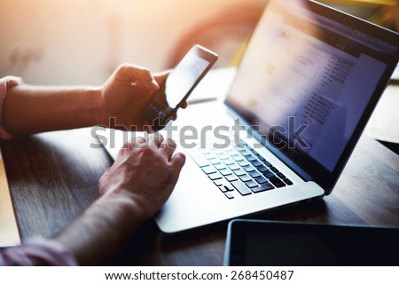 Side view shot of a man\'s hands using smart phone in interior, rear view of business man hands busy using cell phone at office desk, young male student typing on phone sitting at wooden table, flare