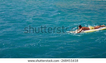 Male surfer floating on his surfboard in the waves of clean bight water, surfer man paddles out through the waves, handsome man enjoying a surf in clear blue water, sexy man surfing at the beach