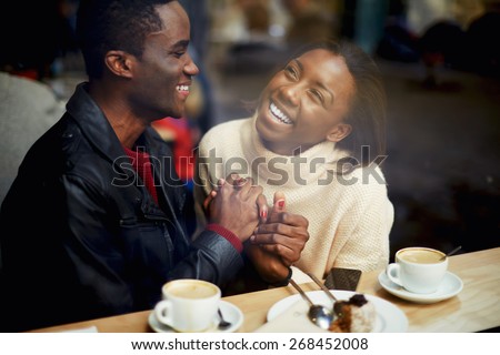 Laughing young couple in cafe, having a great time together, view through cafe window, romantic couple having fun together, best friends smiling sitting in cafe, view through cafe window
