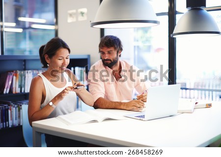 Asian college student taking picture of textbook with her cell phone while sitting in university library,business colleagues at work having fun laughing, couple of freelancers working at modern office