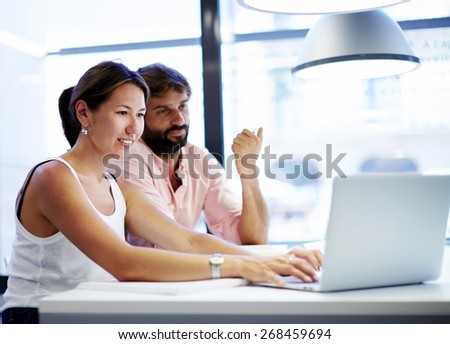 Couple of young office professionals talking over a laptop computer, two business people discussing ideas in co-working space with a laptop or notebook in front of them, students working with laptop