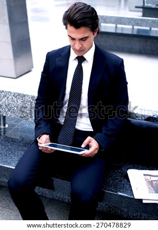 Confident man using digital tablet computer while sitting on the bench in hall of railway station,successful businessman on way to work reading news on his touch pad, executive receiving news on email