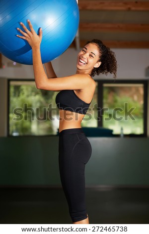 Beautiful young woman enjoying time at the gym, cheerful afro woman laughing while hold fit ball in health center, a radiant young black woman smiling brightly at fitness class