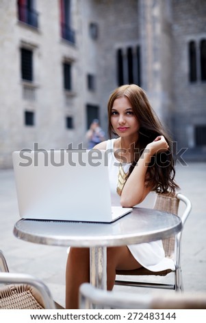 Charming young woman sitting with open laptop computer at cafe table outdoors, female freelancer working on notebook in sidewalk cafe, businesswoman surfing the net while having work break