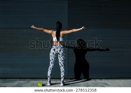 Rear view sporty woman with perfect figure and buttocks stretching her arms against wall with copy space for your text message, fit female in sportswear exercising on black background outdoors