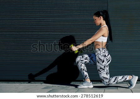 Young fit woman with strong body and perfect figure exercising with dumbbells outside on black wall background, athletic female toning with weights standing against copy space for your text message