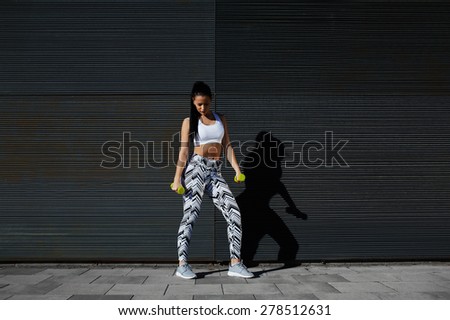 Healthy woman at strength training with dumbbells against black line background outdoors, athletic female holding weights while posing against wall with copy space for your text message