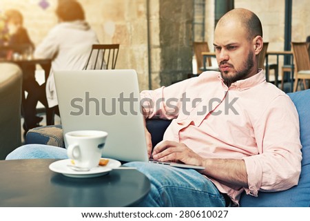 Successful businessman sitting on sofa front open laptop computer and cup of coffee or tea, young freelancer work on notebook in modern coffee shop or hotel interior, make money on-line, e-business