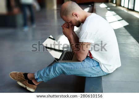 Thoughtful businessman sitting with open laptop computer looking frustrated, male freelancer with notebook sitting in modern space hall looking pensive and worried while thinking about planning