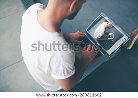 Back view photographer retouching image with him, male designer working on laptop computer while sitting in modern interior,freelancer making money on the distance working on notebook