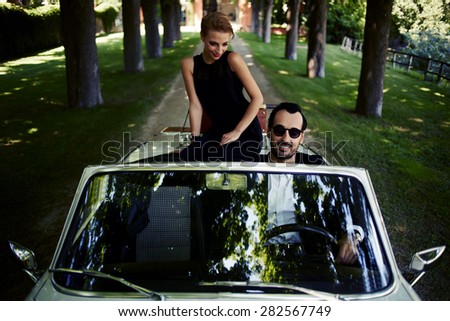 Happy couple enjoying a ride on their luxury convertible in the summer,gorgeous rich woman feels so glad while they riding on cabriolet with sure handsome brunette man, romantic couple at journey trip