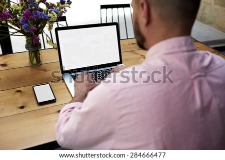 Male person sitting front open laptop computer and smart phone with blank empty screen for your information or content,modern businessman work in internet via notebook, student at coffee shop learning