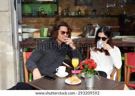 Charming young woman sitting in sidewalk cafe and breakfast with her best friend,two people enjoying and spending time together at pleasant conversation,couple of tourists taking break after city walk