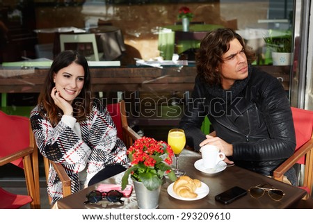 Two student friends drinking cafe after university classes in a restaurant terrace outdoors at cold spring day while they enjoying warm tea and a delicious cake, young couple breakfast in coffee shop