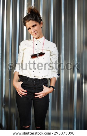 Glamorous young female hipster dressed in a classy modern clothes standing on a shiny metal background with copy space for your text message or content and look to the camera on a sunny summer day