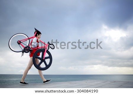 Full length portrait of stylish woman dressed in sport suit holding her light weight fixed gear bike while walking along concrete pier, hipster girl stroll with bicycle at seashore with copy space sky