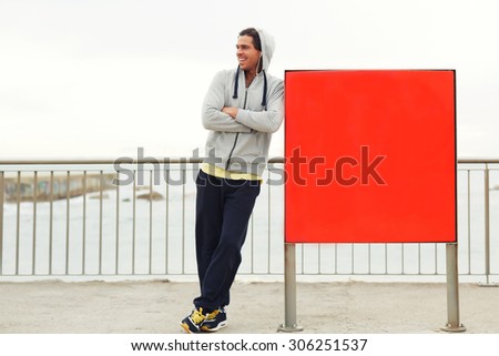 Full length portrait of smiling male jogger taking break after an active run outdoors while standing near a red board with copy space area for text message or content,sportsman resting after training