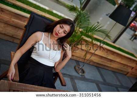 Portrait of a wonderful asian woman relax while sitting at cafe terrace, young charming model posing for the camera in open air coffee shop during her recreation time