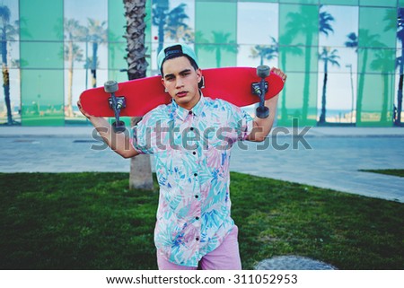 Stylish hipster man with cup on the head standing in beautiful park after be ridden onÂ  skateboard