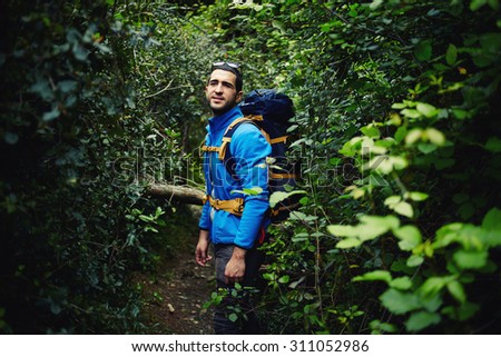 Young hiker with backpack walk in tropical jungle while enjoying wild nature landscape, traveler standing on forest trail against green plants with copy space area for your text message or information