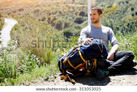 Tired hiker with backpack resting after active walk in mountains, traveler man enjoying scenery landscape view on top of hill with copy space area background for your text message or advertise content