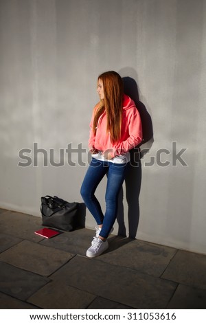 Full length portrait of stylish teenager girl dressed in modern clothes standing near cement wall background with copy space for your text message or advertising,female hipster standing alone outdoors