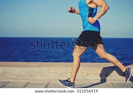 Cropped shot with muscular build man running along the seashore with copy space area for your text message or advertising content, male jogger working out outdoors o the beach at sunny afternoon