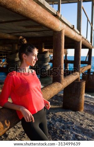 Half length portrait of attractive young female runner having rest after an active morning jogging along the beach, charming runner woman taking break after exercising in sunny summer morning outdoors