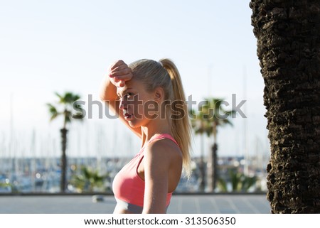 Young charming female runner holding hand above her forehead while taking a break after fitness training outdoors, tired athletic woman in sportswear rest after fitness training in the fresh air