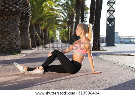 Portrait of a young fit woman dressed in sportswear taking break after active physical exercises outdoors, athletic female in sport bra enjoying rest after fitness training outside in sunny summer day